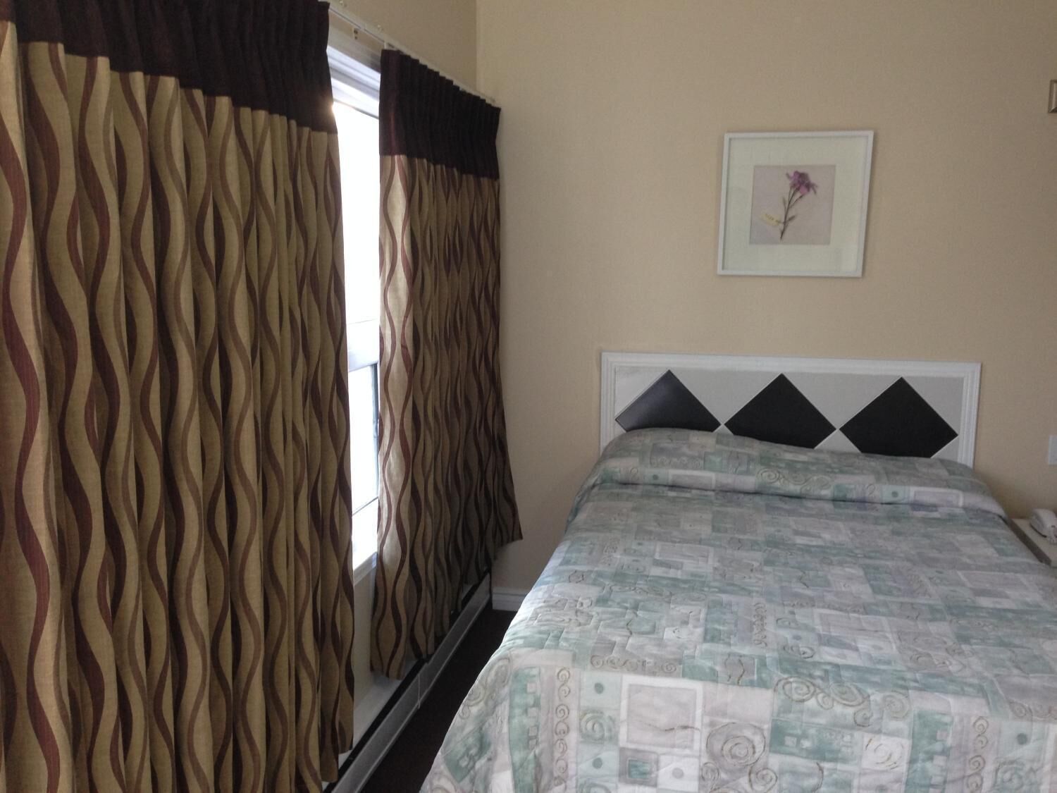 Een slaapkamer met een bed, gordijnen, een ingelijst beeld aan de muur en een raam.