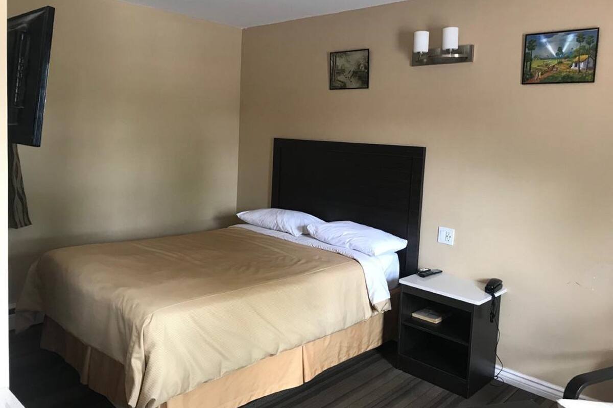 A hotel room with a bed, bedside table, and a small desk with a chair.