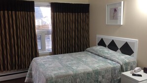 Una habitación de hotel con una cama, una mesita de noche con teléfono y control remoto, y una ventana con cortinas.