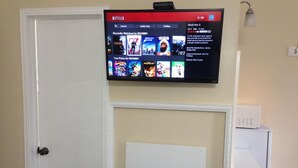 Un televisor montado en la pared muestra la interfaz de Netflix con varias categorías y una selección de películas.