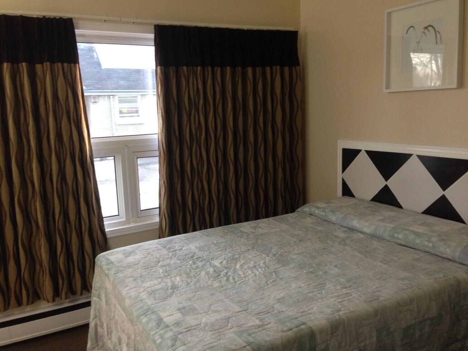 A room with a bed, a window with curtains, and a wall-mounted picture.