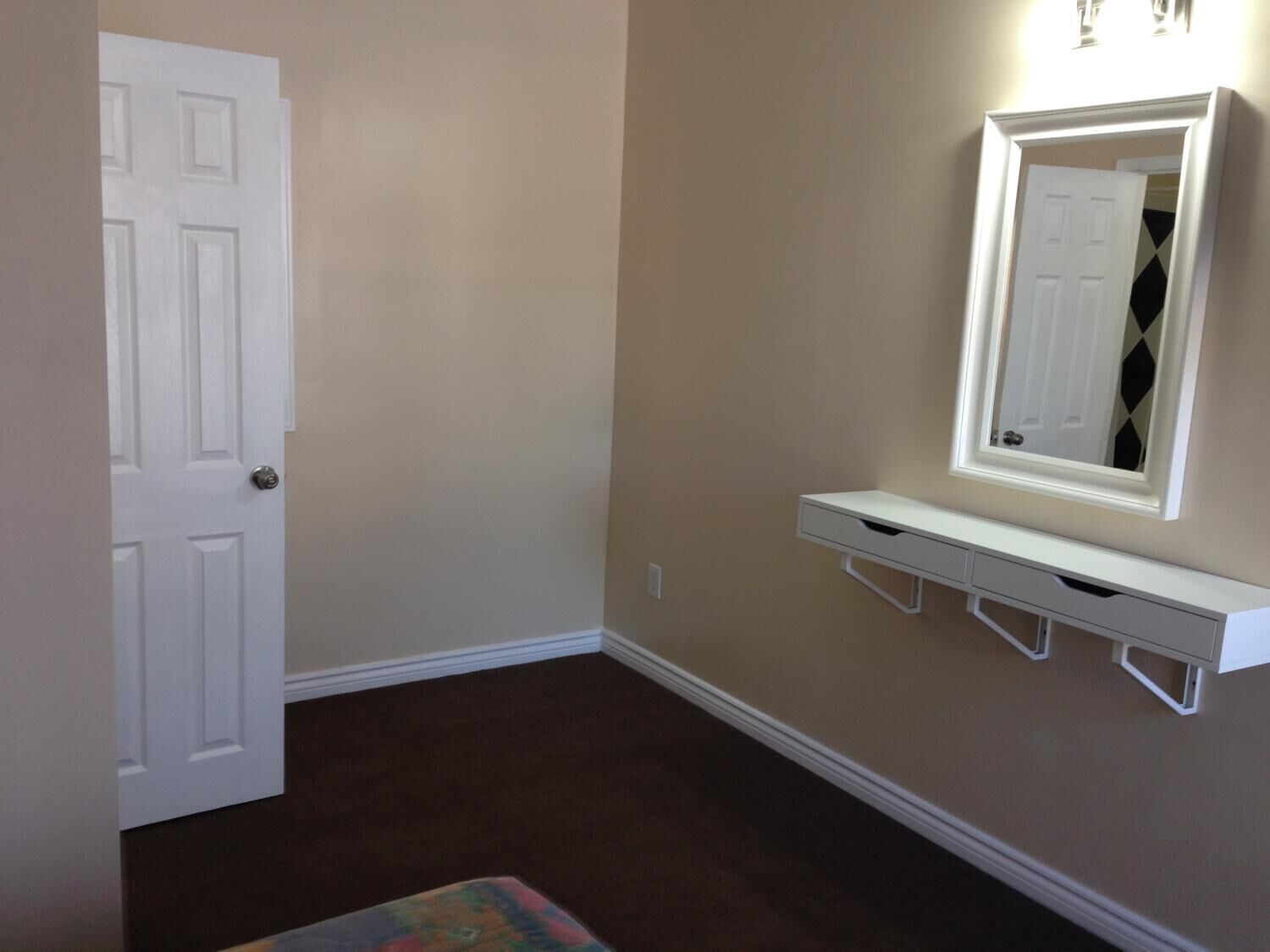 A hallway with a white door, a white console table with a mirror, and a brown carpet.