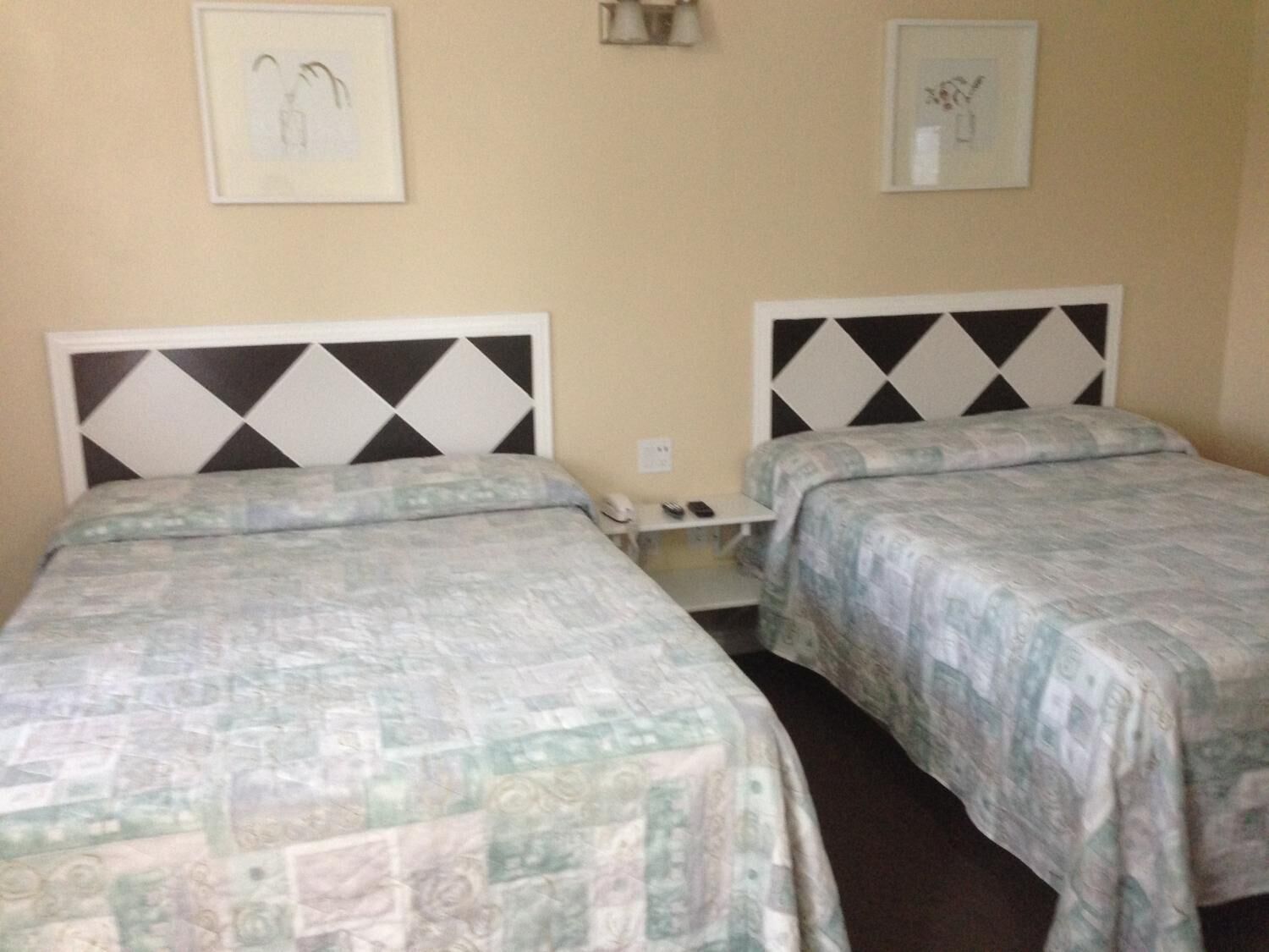 A hotel room with two beds, each with a patterned bedspread, a bedside table with a lamp, and framed artwork on the walls.