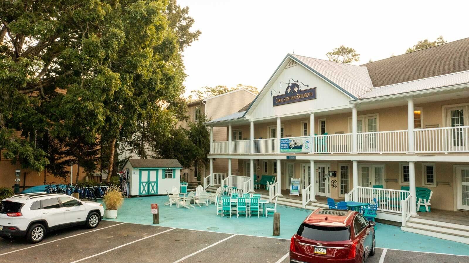 A two-story building with a covered porch, outdoor seating, and a small adjacent structure.