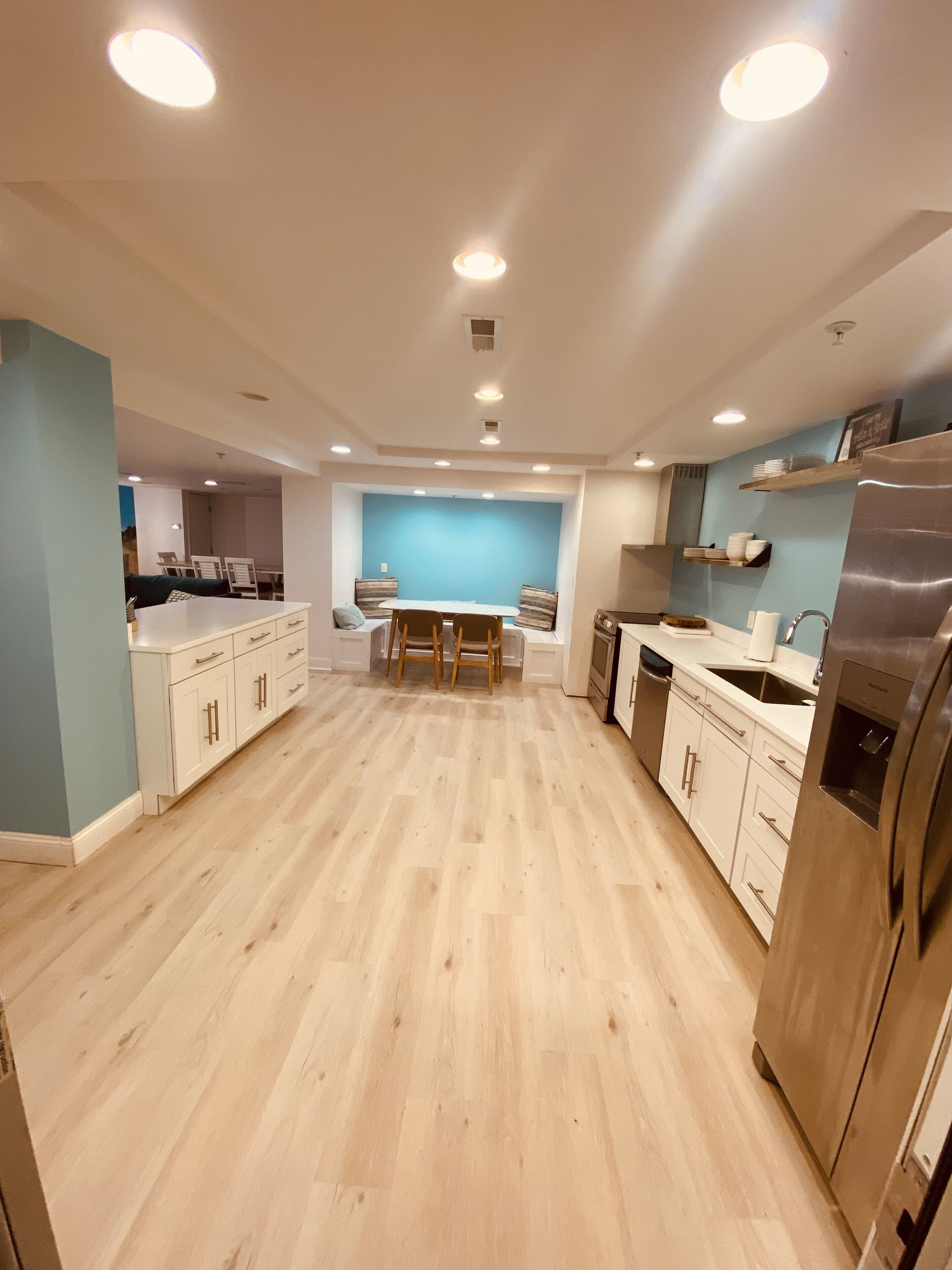 Una cocina moderna con suelo de madera, armarios blancos, un refrigerador de acero inoxidable y luces empotradas en el techo.