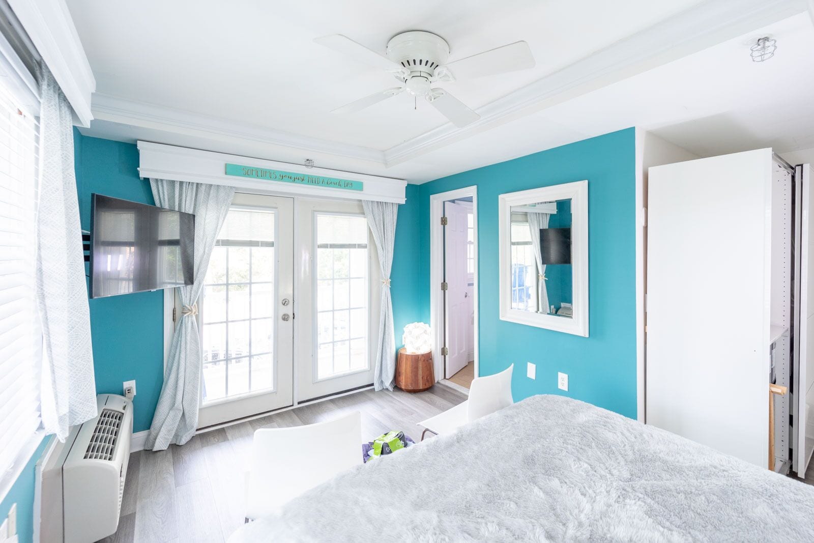 Un dormitorio con cama, ventilador de techo, televisor y ventana con cortinas.