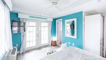Un dormitorio con cama, ventilador de techo, televisor y ventana con cortinas.