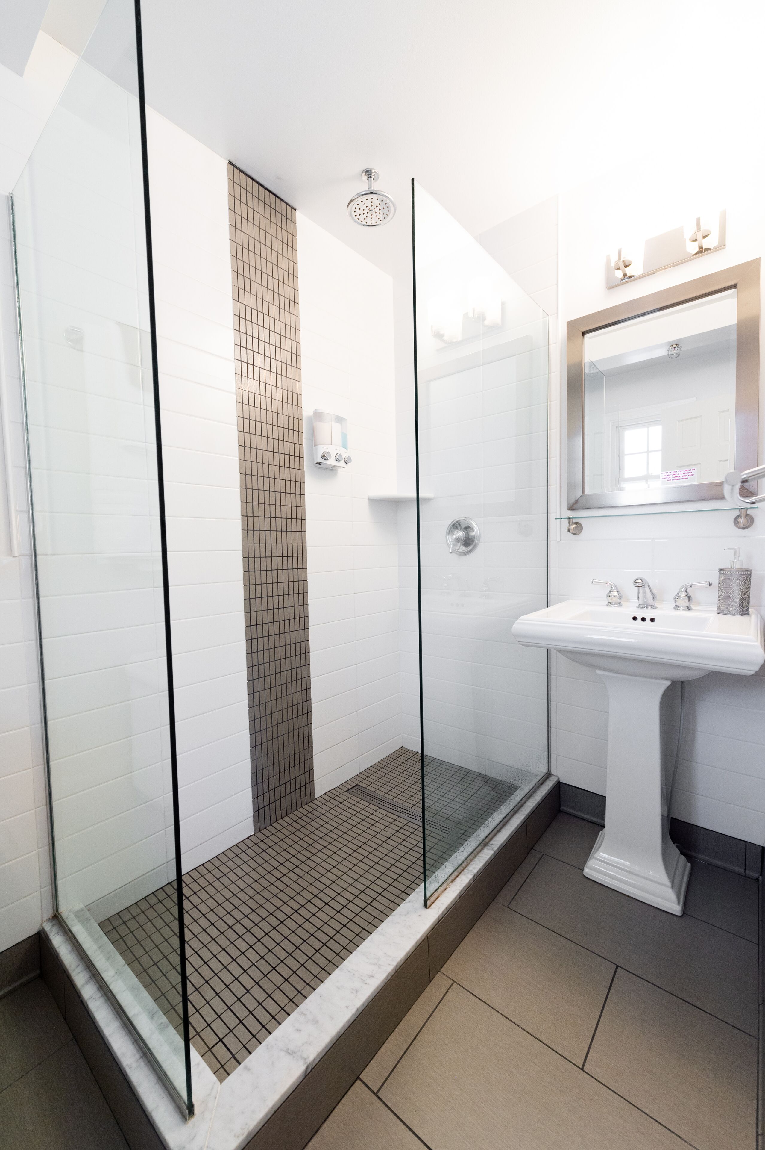 A modern bathroom with a glass-enclosed shower, a white sink, and a tiled floor.