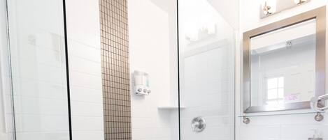 A modern bathroom with a glass-enclosed shower, a white sink, and a tiled floor.