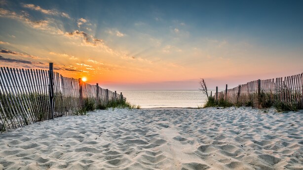 Una playa arenosa con una valla de madera que conduce al océano al atardecer.