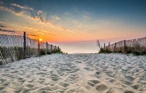 A sandy beach with a wooden fence leading to the ocean at sunset.