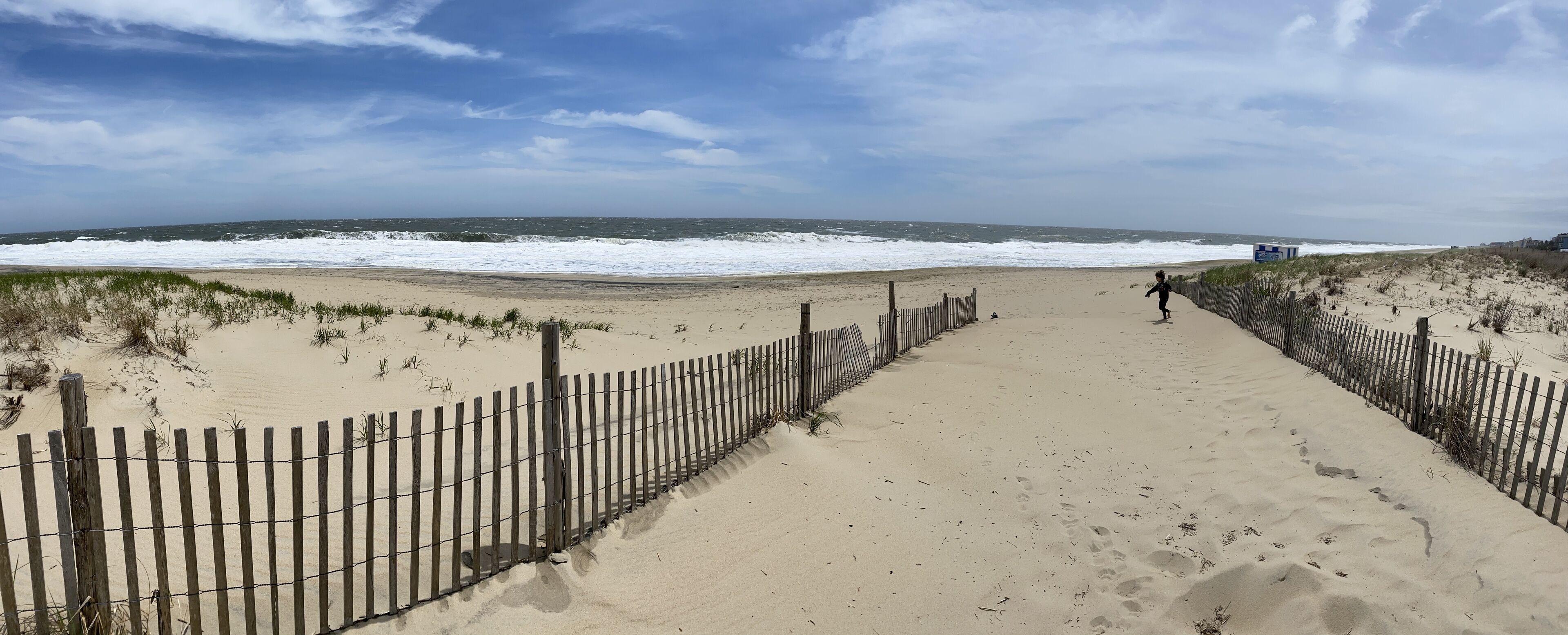 A sandy beach path with a wooden fence on both sides, leading to the ocean.