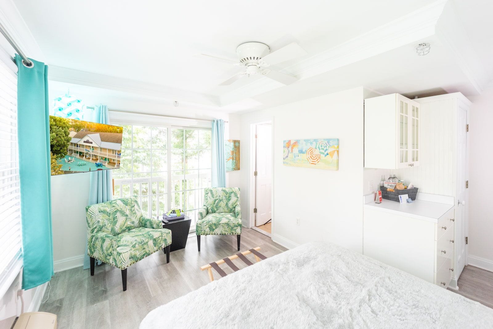 Una habitación luminosa con una cama, dos sillas, una mesita, un cuadro y vista a una casa a través de la ventana.