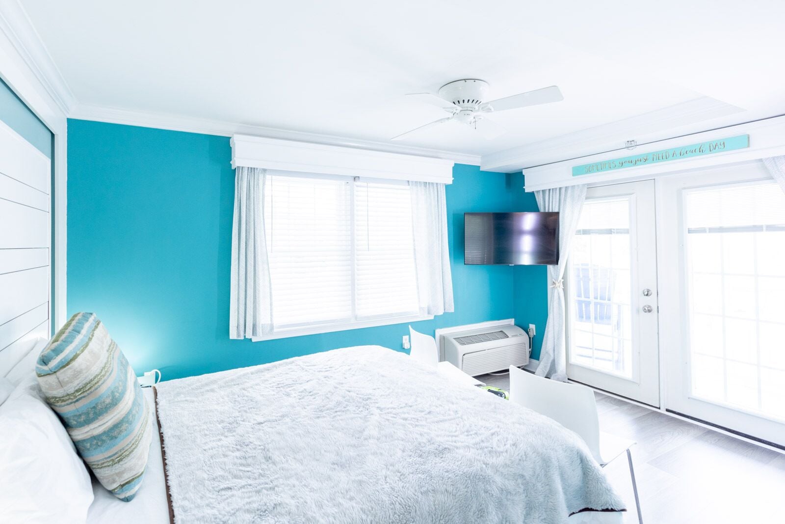 A bright room with a bed, a ceiling fan, a TV, and a window with curtains.