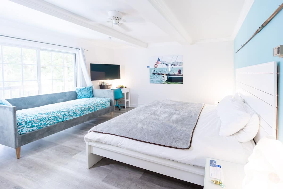 A modern bedroom with a bed, a sofa bed, a desk, and a window.