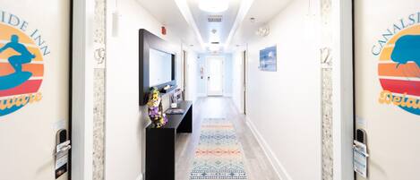 A hotel corridor with a reception desk, a TV, and a patterned rug.