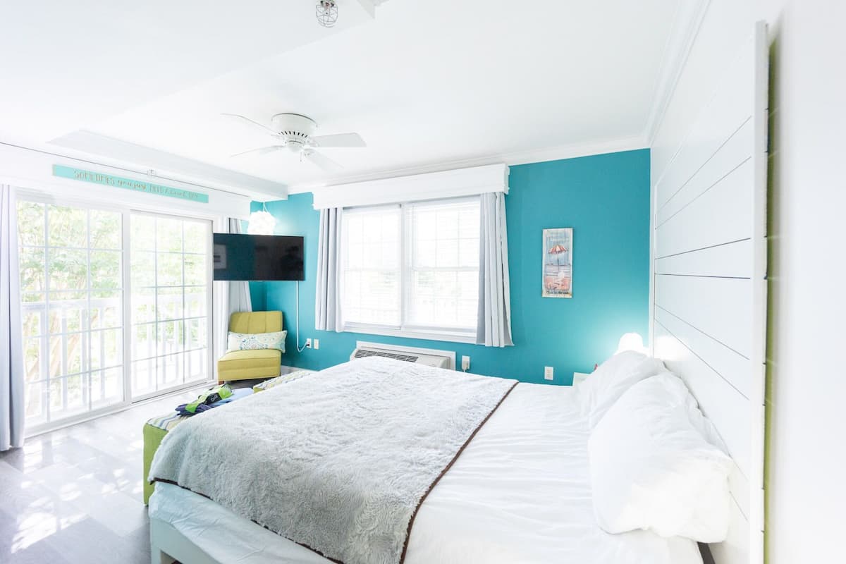 A bedroom with a bed, a ceiling fan, a TV, and a window with curtains.