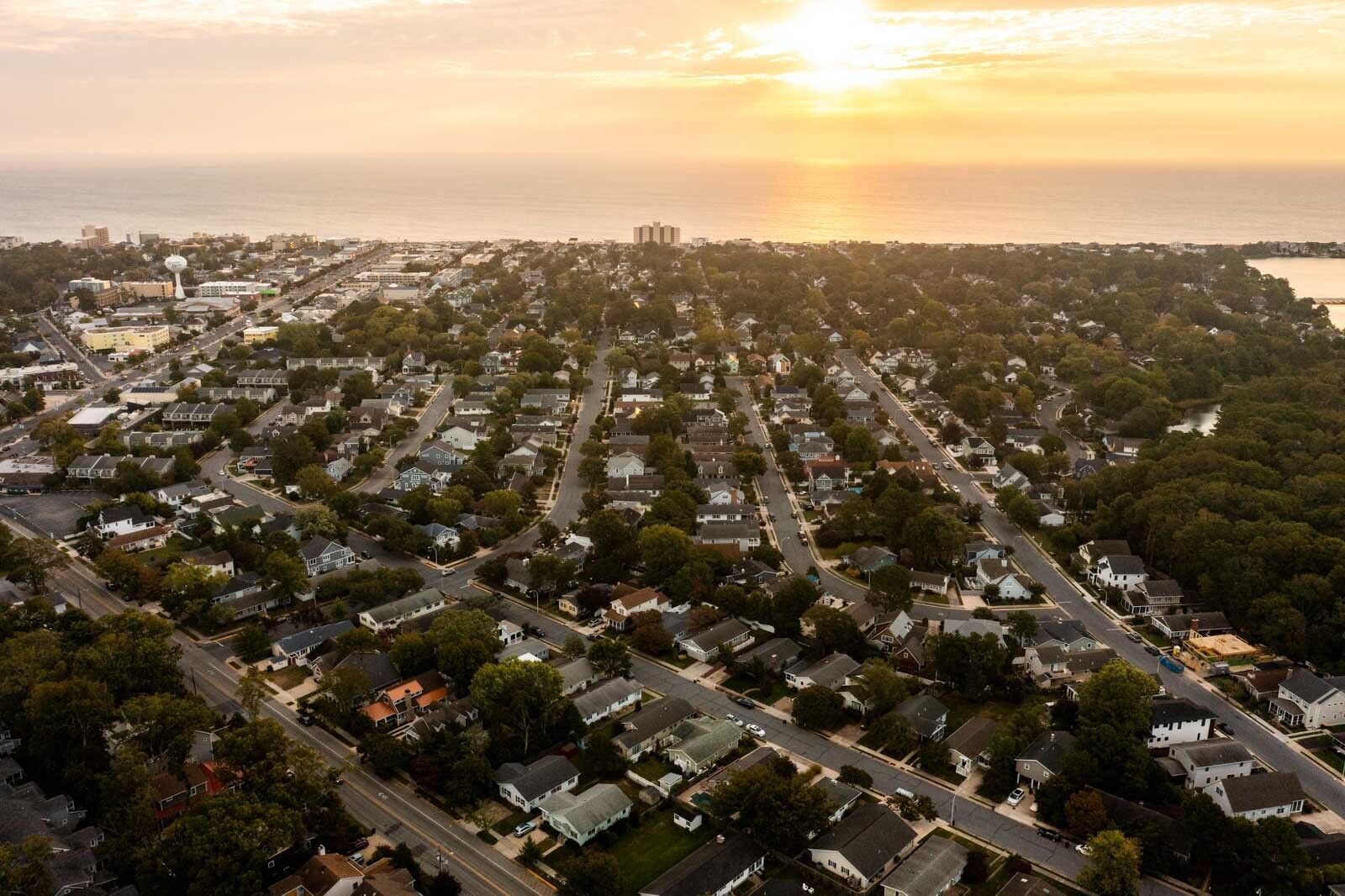 An aerial view of a residential area with houses, streets, and a water body in the background.