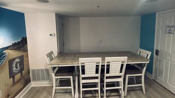 Un comedor con una mesa de madera y sillas blancas, un mural en la pared y una puerta con el letrero 'Staff Only'.
