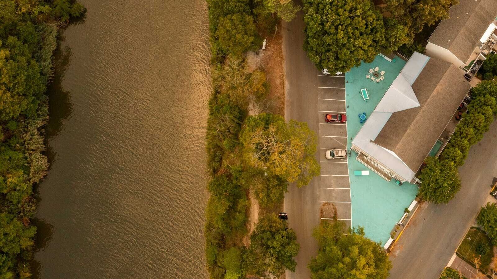 An aerial view of a hotel with a swimming pool, parking lot, and adjacent forested area.