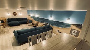 Una sala de estar moderna con una gran mesa de comedor de madera, un sofá seccional azul y un mural de una playa.