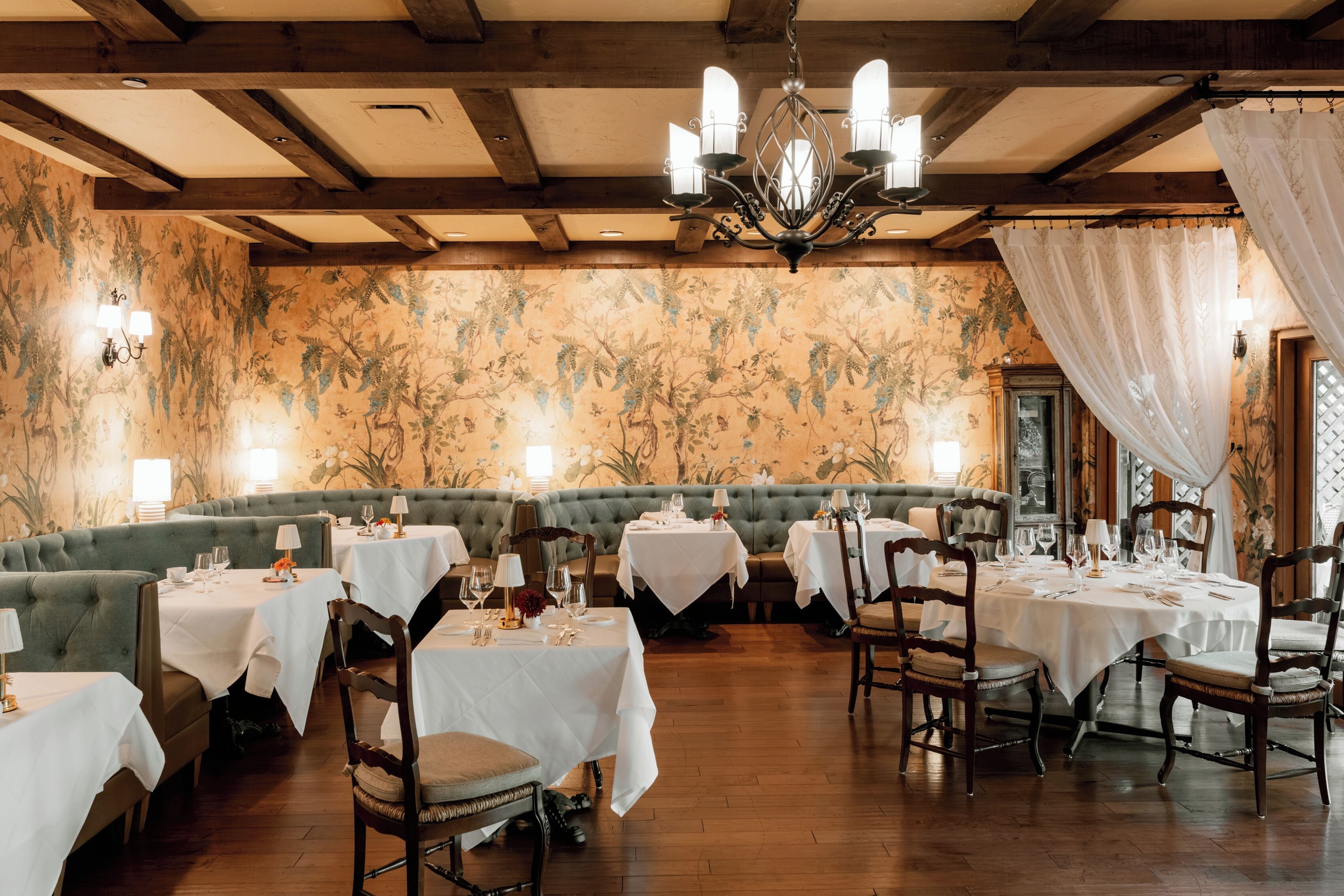 A restaurant with round tables, green cushioned seating, and a floral wallpaper interior.