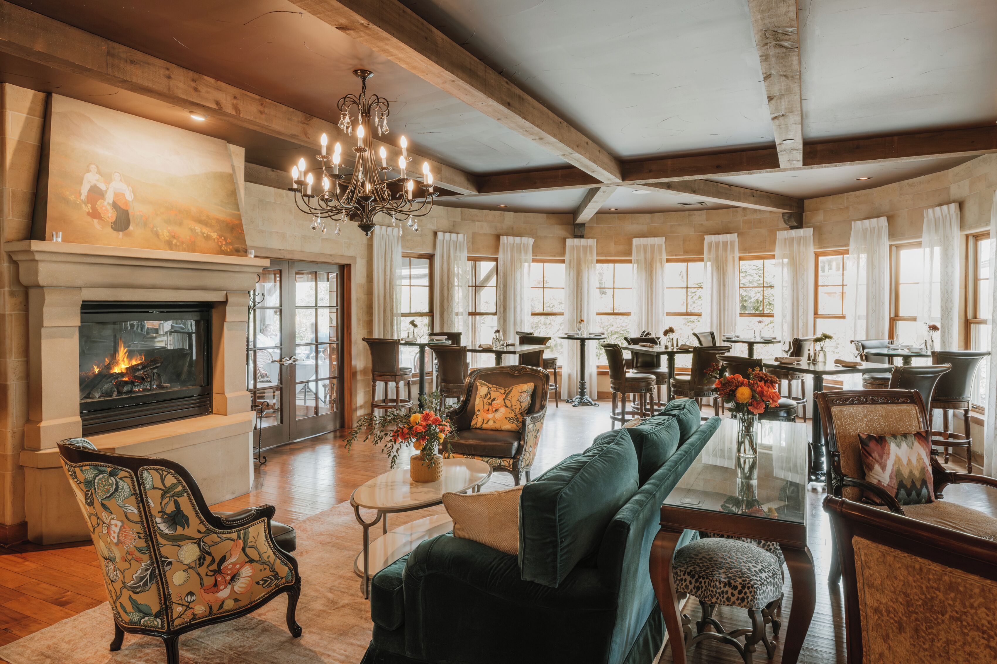 A spacious living room with a fireplace, wooden beams, a chandelier, and a dining area with tables and chairs.
