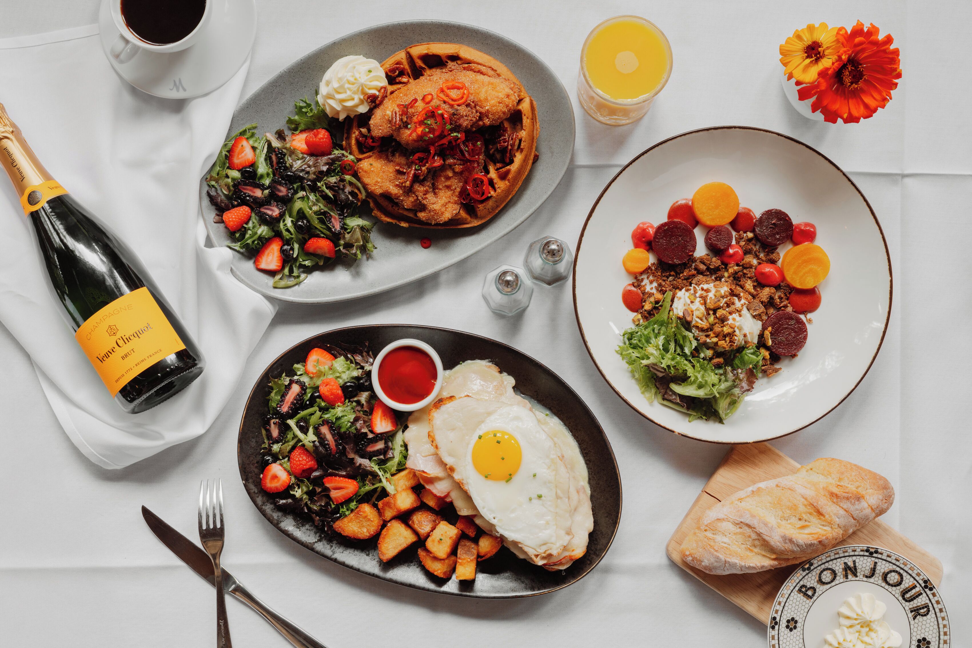 A table with plates of food, a bottle of champagne, and a glass of juice.