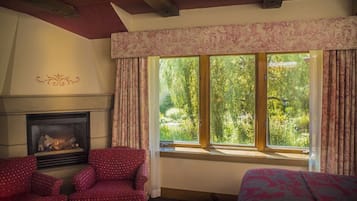 A room with a fireplace, two patterned armchairs, a bed, and a large window with curtains.