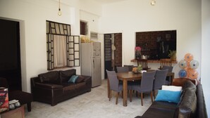 Una sala de estar con sofá de cuero marrón, una mesa de comedor con sillas, un refrigerador y una zona de cocina con salpicadero de azulejos.