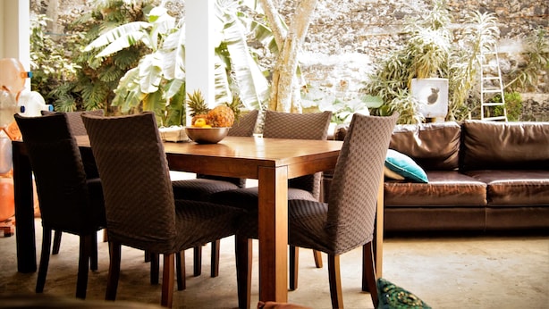 Un comedor con una mesa y sillas de madera, rodeado de plantas en macetas y un muro de piedra.