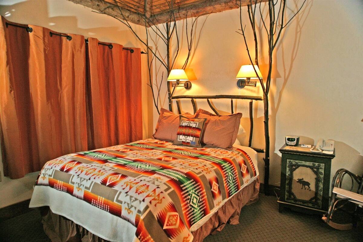 A cozy bedroom with a bed, two wall-mounted lamps, a nightstand, and a decorative wall piece.