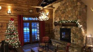 A cozy log cabin interior with a stone fireplace, a Christmas tree, and rustic wooden furniture.