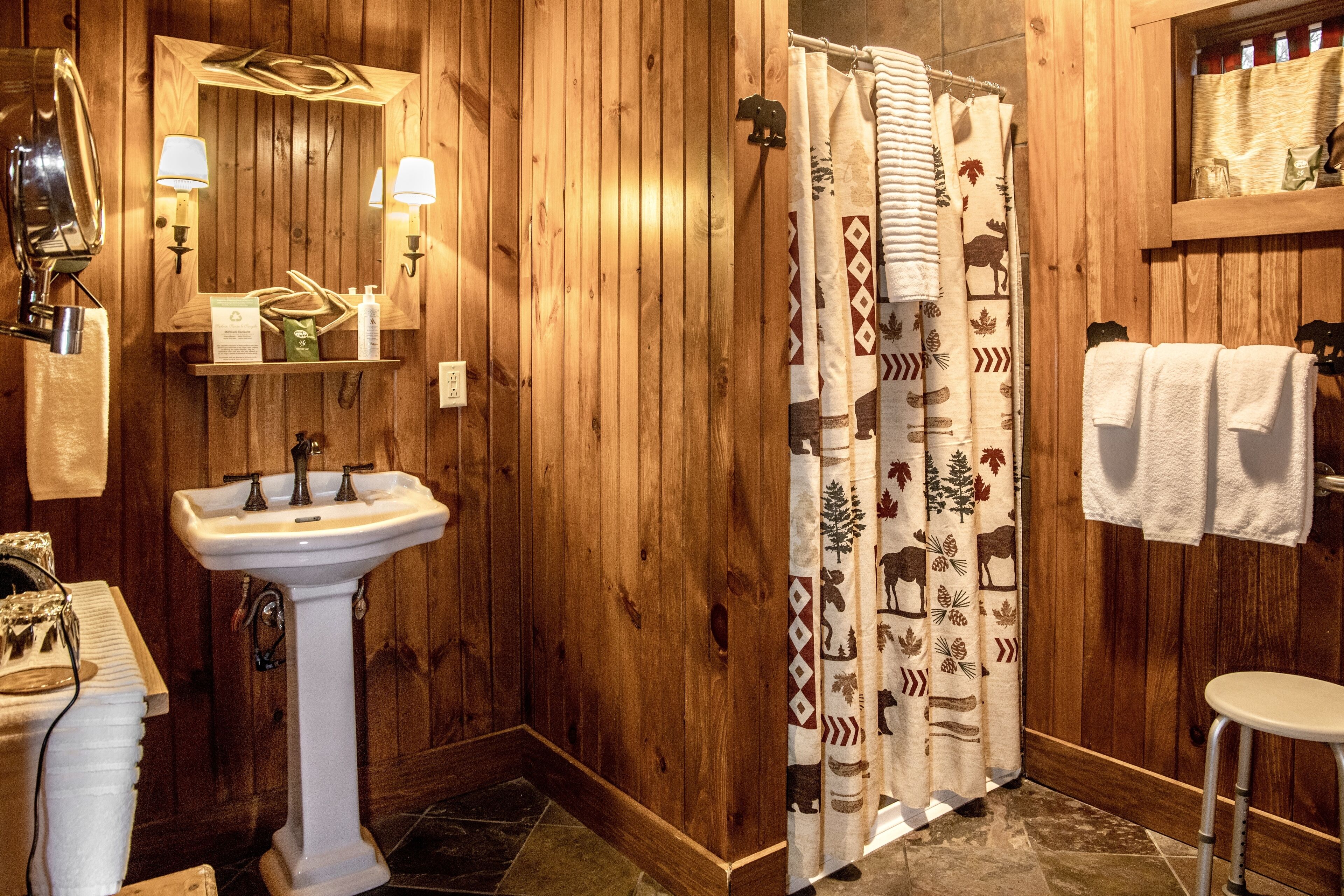 A wooden bathroom with a pedestal sink, a mirror, and a shower curtain with animal prints.