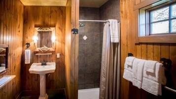 A wooden-paneled bathroom with a pedestal sink, a shower, and a window.