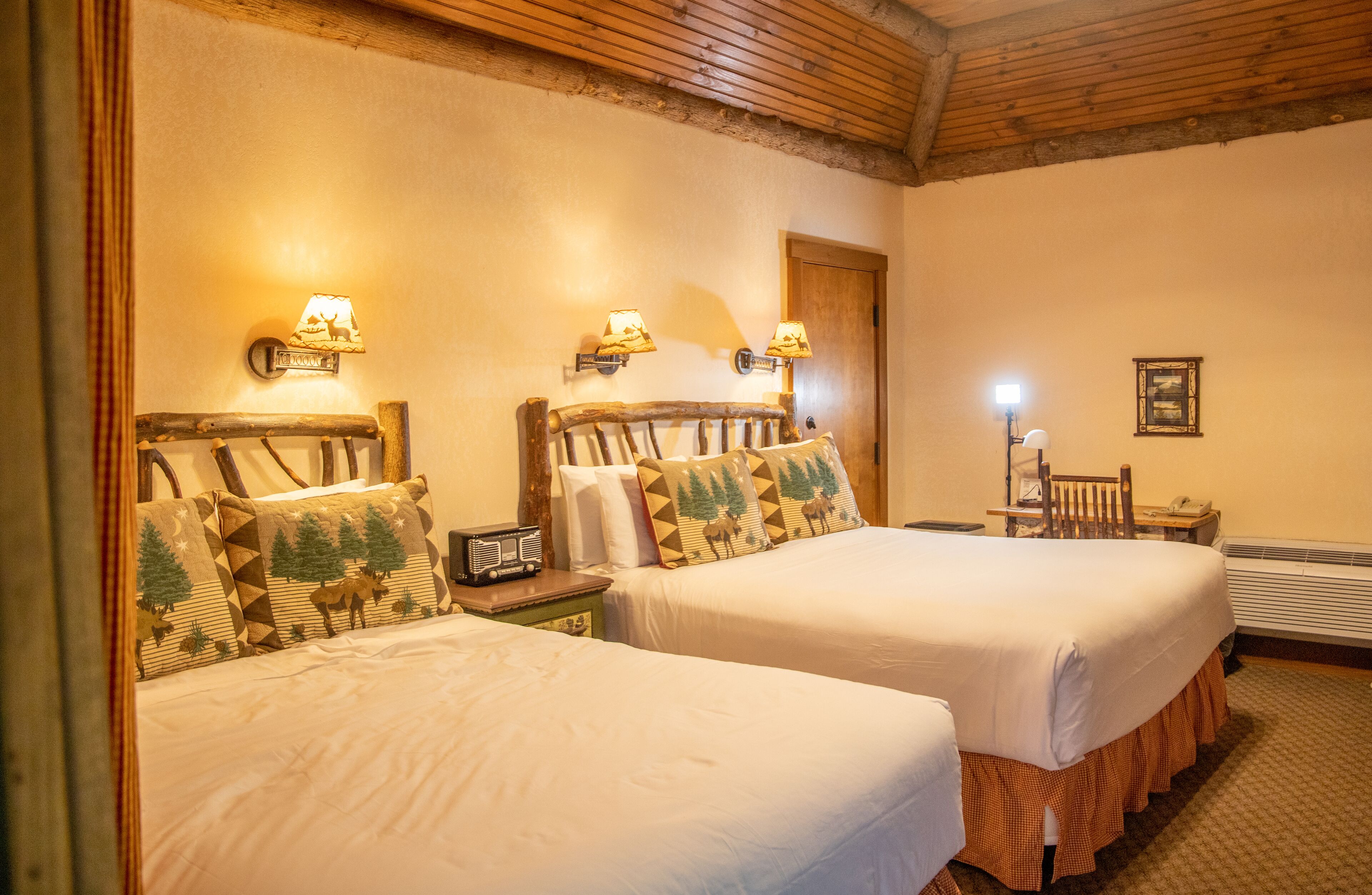 A hotel room with two beds, wooden headboards, and wall-mounted lamps.