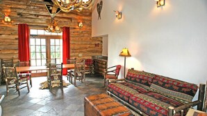 A rustic interior with a wooden dining table, chairs, a sofa, and a lamp.