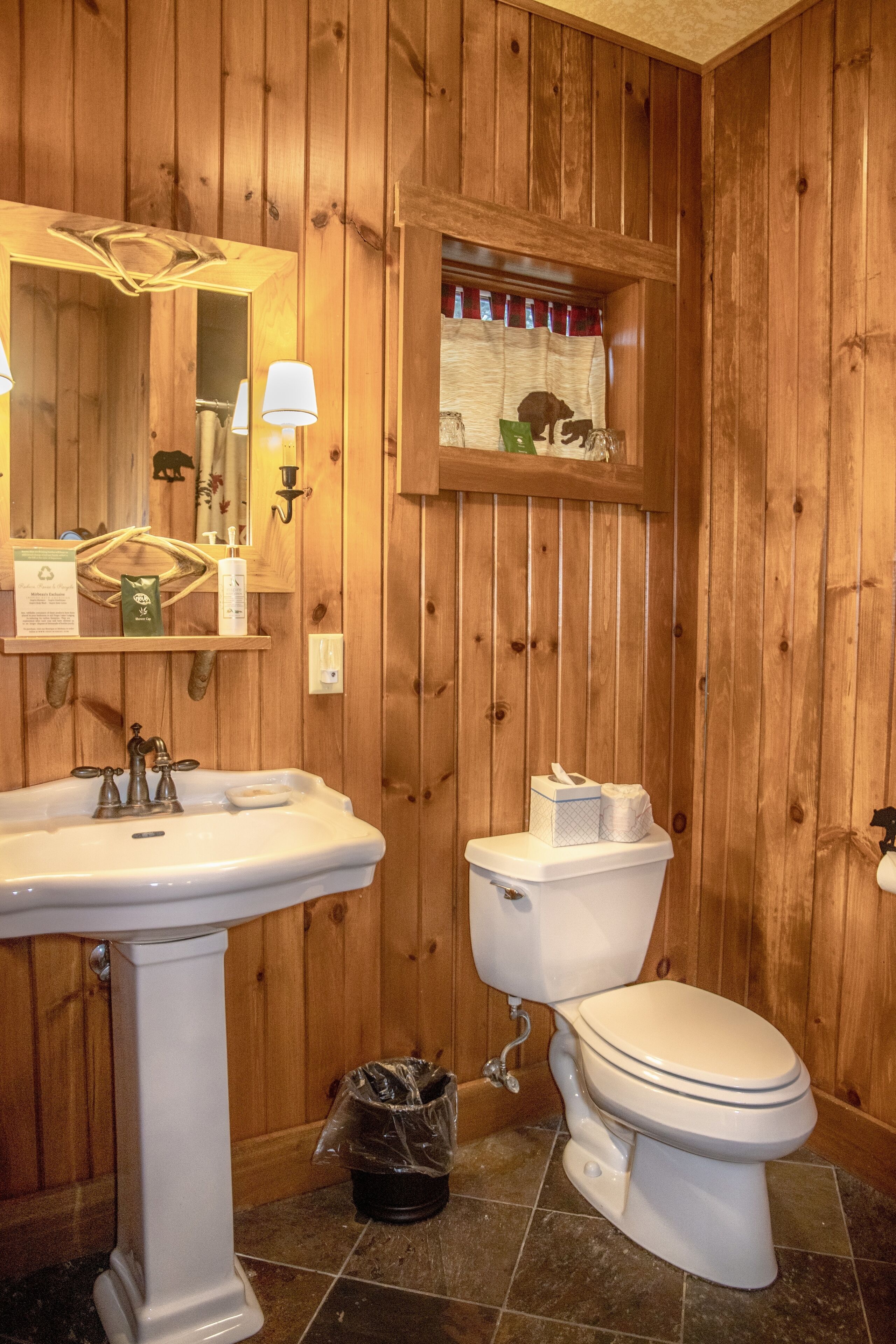 A wooden-paneled bathroom with a pedestal sink, toilet, and a small window with a decorative animal.
