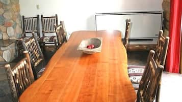 Un comedor con una larga mesa de madera, seis sillas, una lámpara de araña y una pared de piedra.