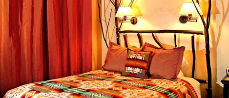 A bed with a patterned bedspread, a headboard with two wall-mounted lamps, and a red curtain.