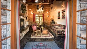 A cozy lodge interior with a stone fireplace, wooden furniture, and a chandelier.
