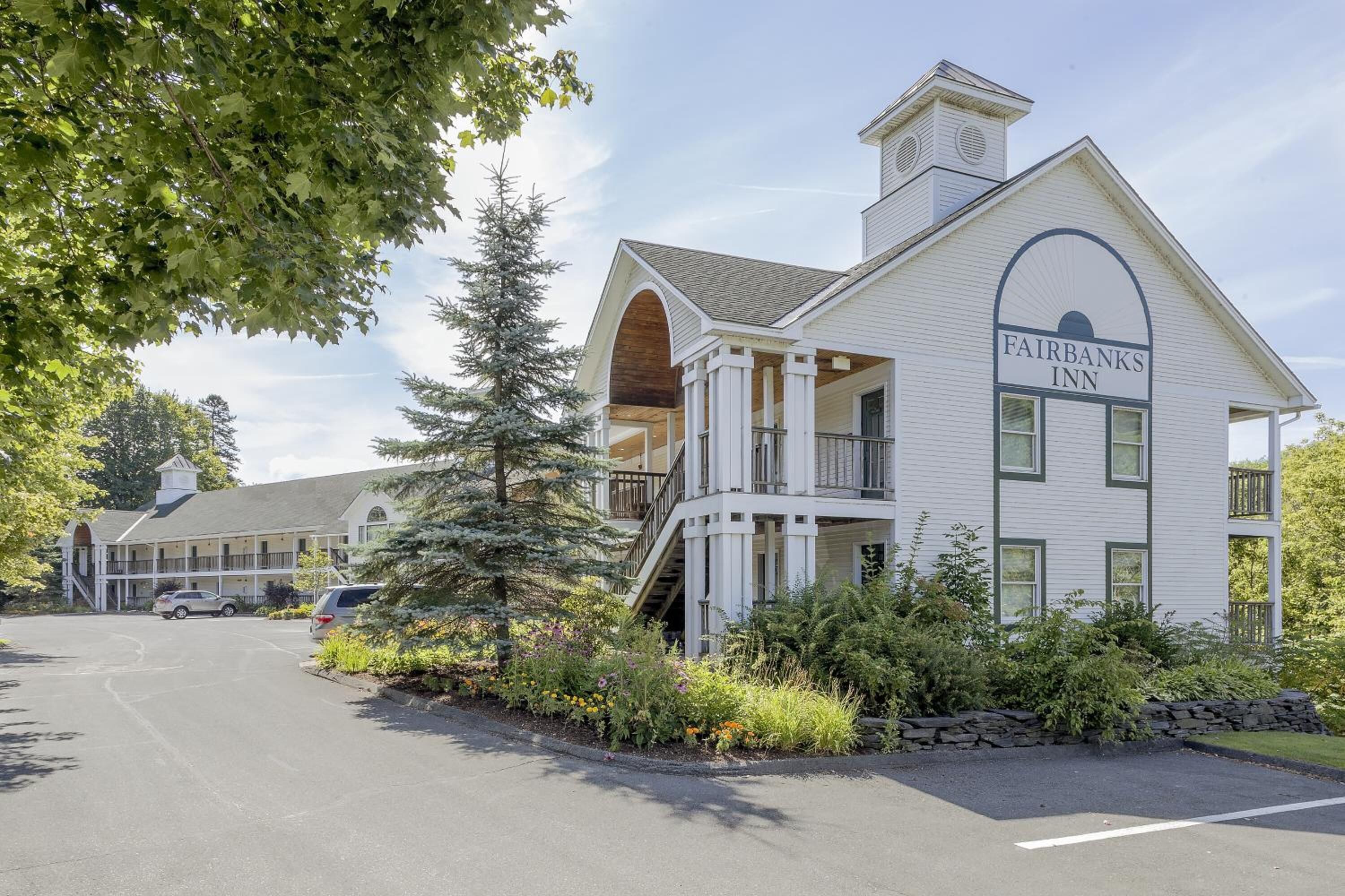 A two-story Fairbanks Inn with a white exterior, a covered porch, and a stone wall garden.