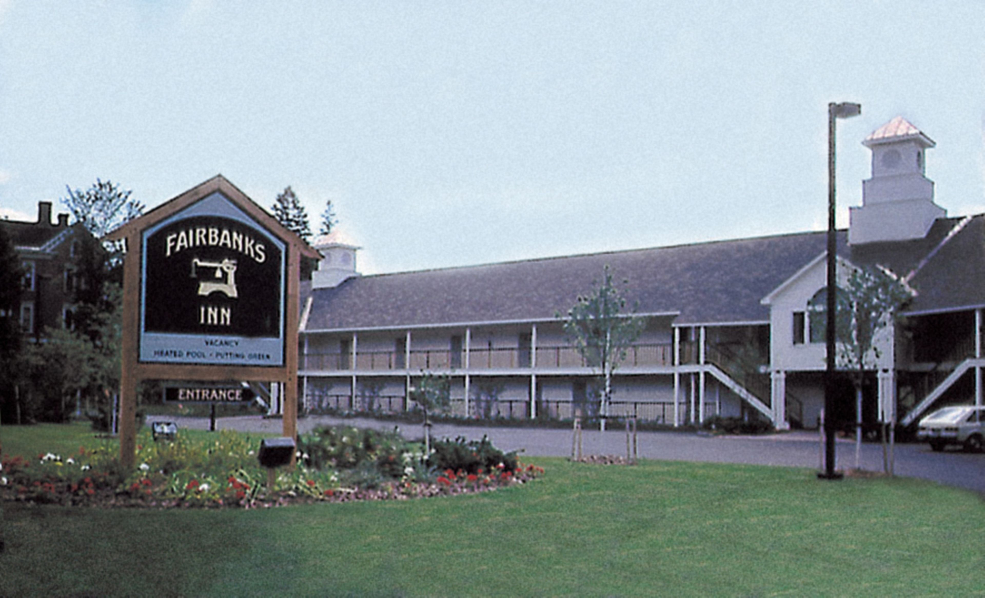 Letrero del Fairbanks Inn con piscina climatizada, un edificio de techo inclinado y un pequeño jardín con flores.