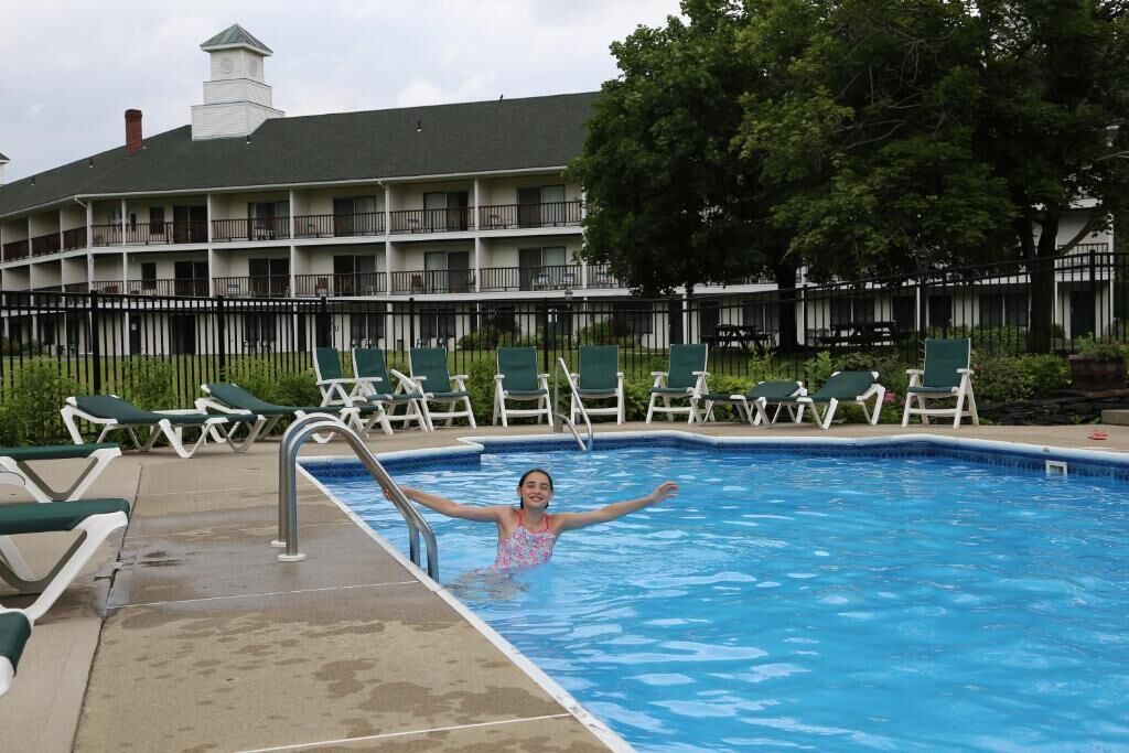 Piscina com espreguiçadeiras e um edifício com varandas ao fundo.