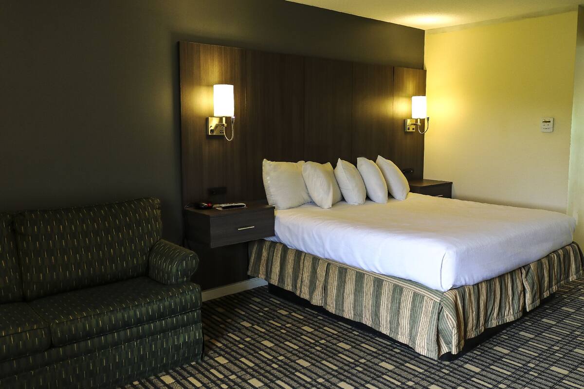 A hotel room with a bed, a sofa, and two wall-mounted lamps.