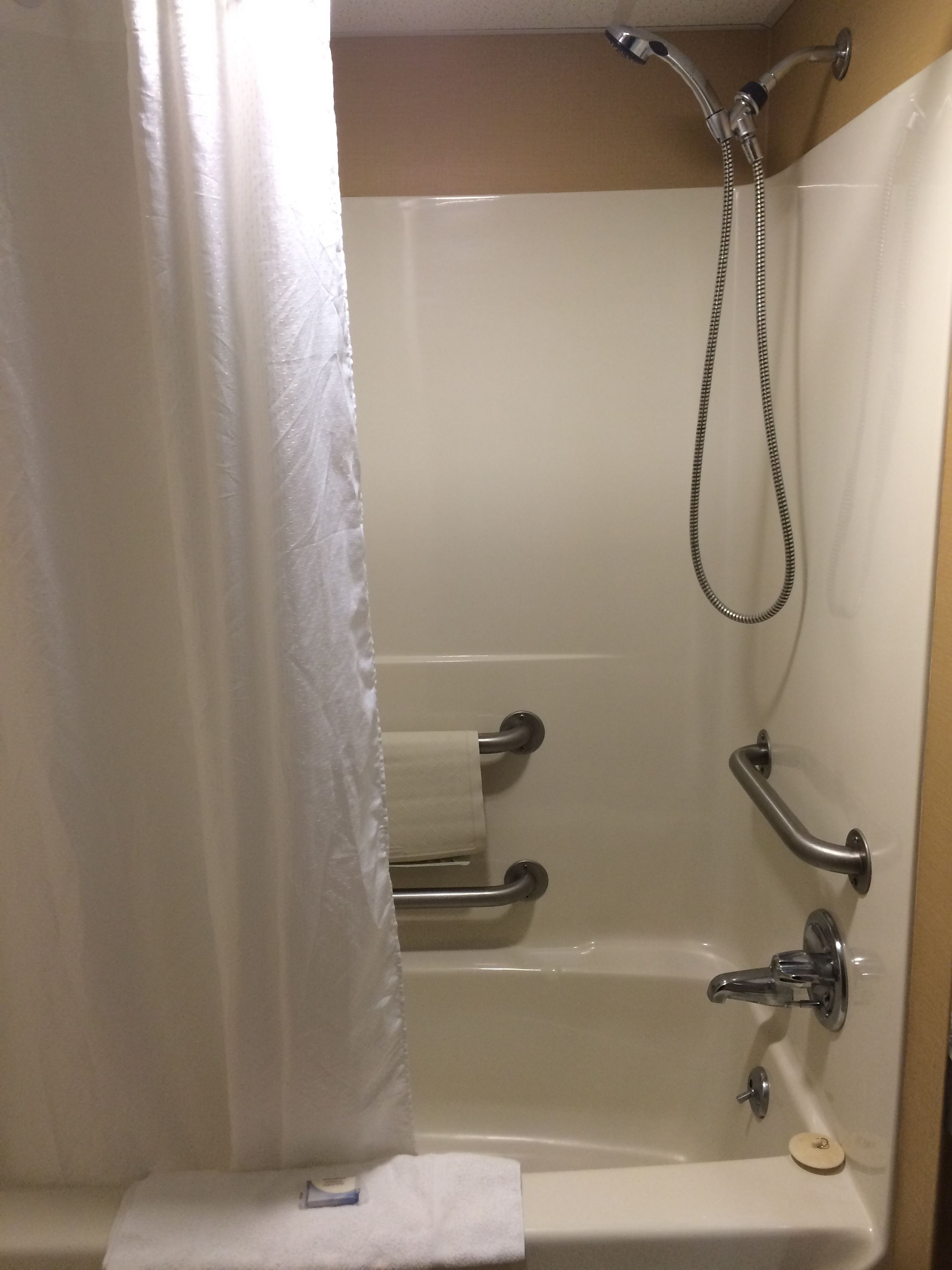 Une salle de bain équipée d’une baignoire, d’une douche et de toilettes. Des barres d’appui sont installées à proximité de la baignoire et de la douche.