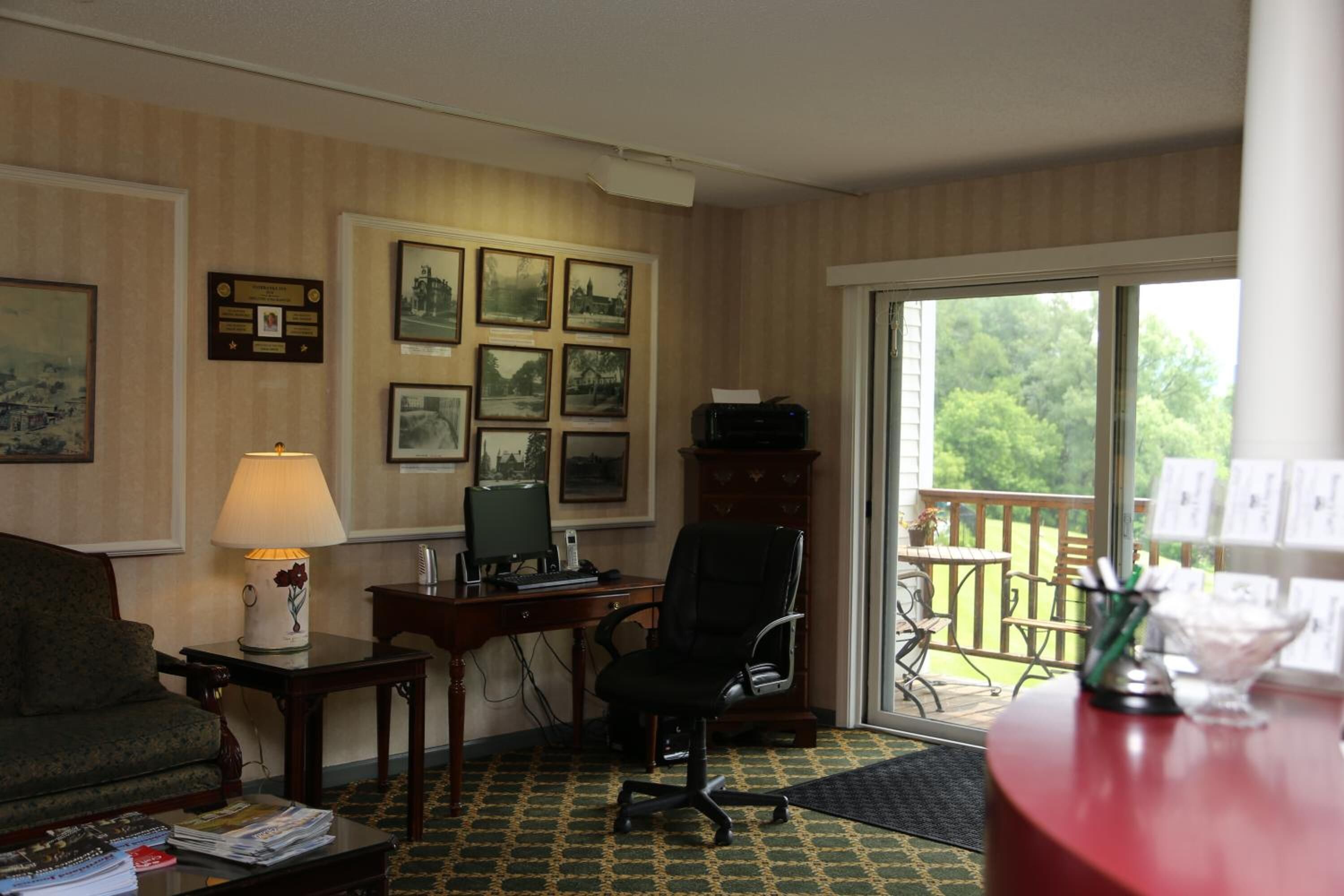A hotel room with a desk, computer, and chair, a sofa, and a view of the outdoors through a sliding glass door.