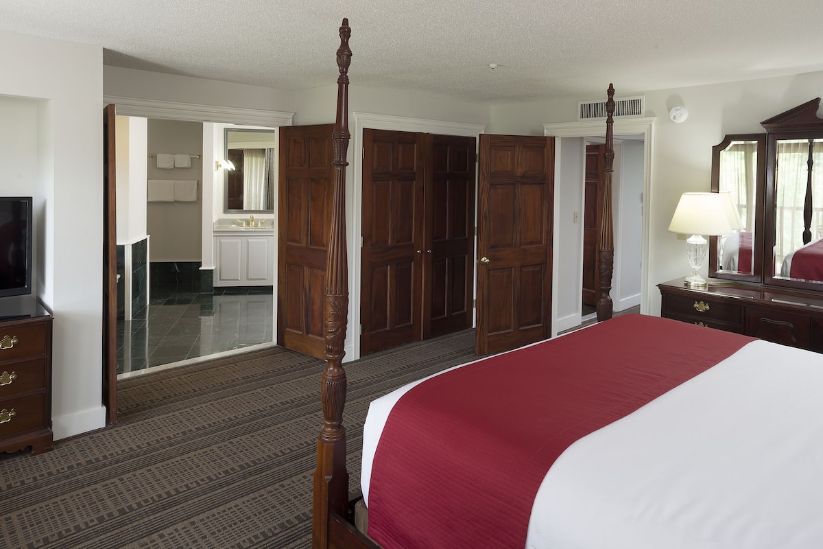 A hotel room with a four-poster bed, wooden wardrobe, a mirror, and a television.