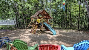 Ein Spielplatz mit einem hölzernen Spielhäuschen und einer Rutsche, umgeben von Bäumen.