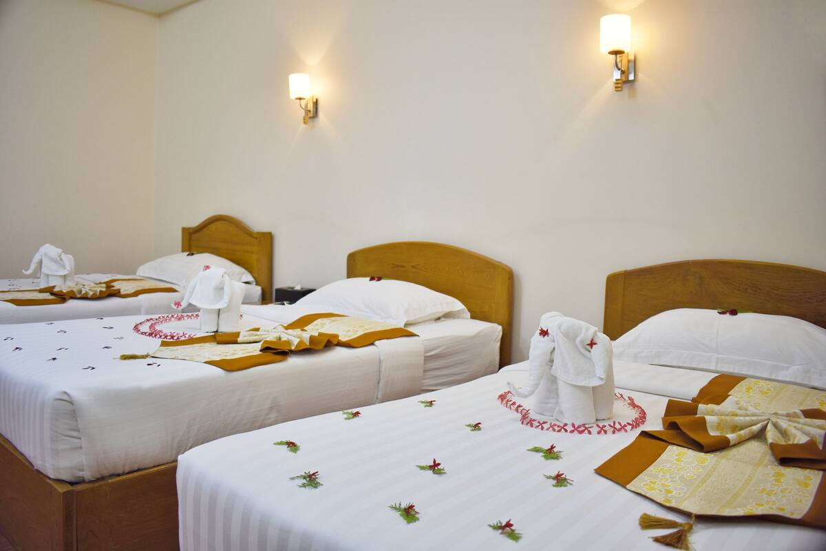 Ein Hotelzimmer mit drei ordentlich bezogenen Betten, jedes mit weißer Bettdecke und einem dekorativen Kopfkissen.